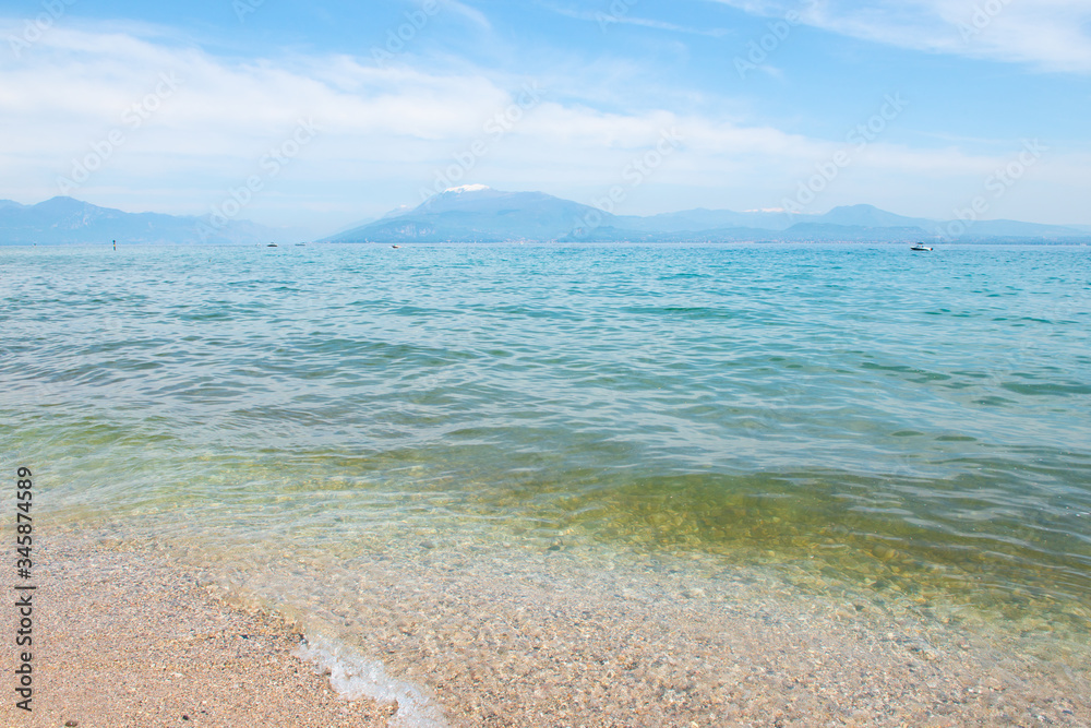 Obraz premium Landscape with blue sky, mountains and transparent blue turquoise water in lake Garda, Sirmione del Garda, Italy, Europe. Peaceful place
