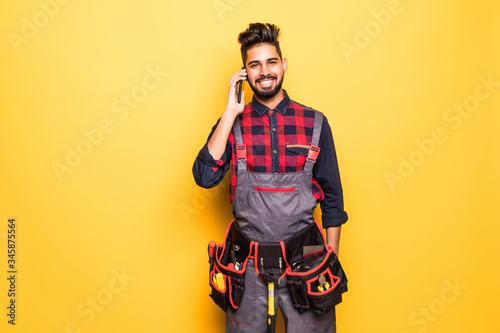 Builder indian construction worker on phone, isolated on yellow background
