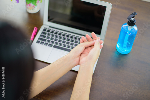 Women who work at home use alcohol gel to wash their hands before typing the computer
