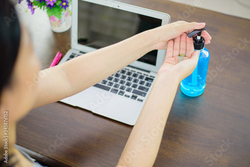 Women who work at home use alcohol gel to wash their hands before typing the computer