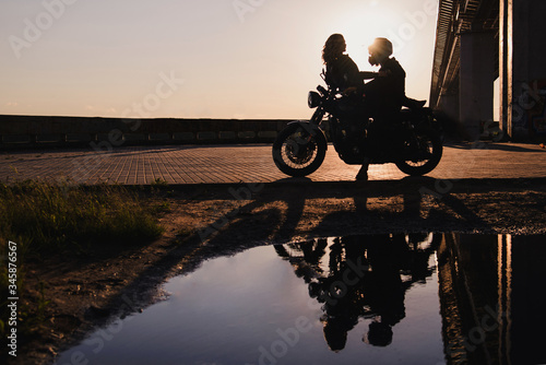 Silhouette of a couple of bikers in love on a motorcycle at sunset in the city landscape.