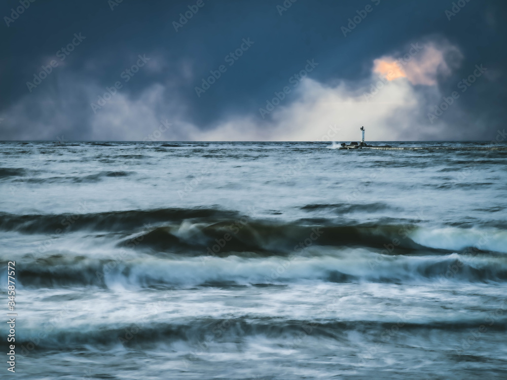 Sea waves of Baltic sea at long exposure. Cloudy sky over the water. White lighthouse.