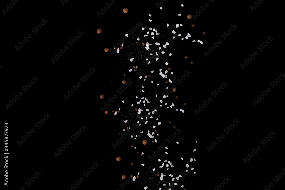 Levitating salt crystals and black pepper spice on black. Copy space Levitating salt crystals and black pepper spice on black. Copy space