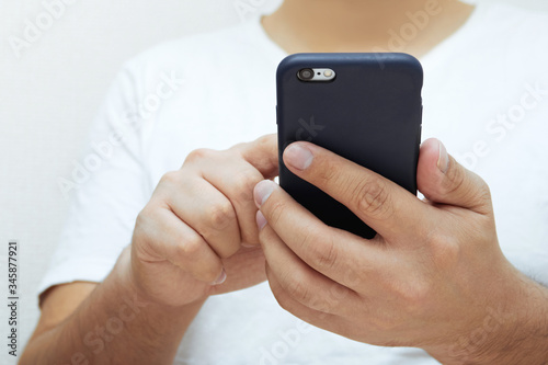 Close-up of a young man holding a smartphone and tapping the screen. Concept of modern electronics and technologies for business and education