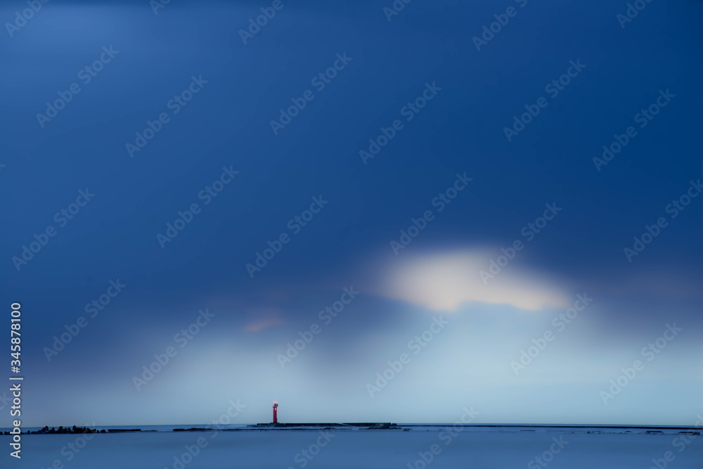 Sea waves of Baltic sea at long exposure. Cloudy sky over the water. Orange lighthouse.