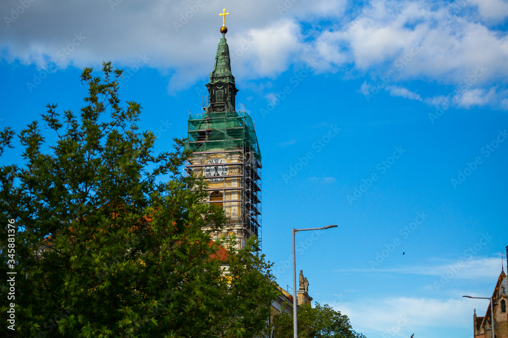 Blue sky and great tonal range clouds, clear weather, church and bell tower covered with a tree at Kecskemét city, Hungary. The temple is currently under construction. Blue sky and great tonal range clouds, clear weather, church and bell tower covered with a tree at Kecskemét city, Hungary. The temple is currently under construction.