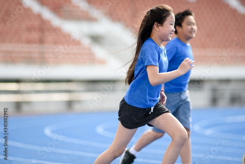 Young Asian boy and girl running on blue track in summer.