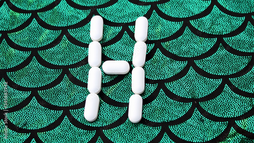 Alphabet made of pills on a green and black background. Vitamins on a background of scales. Abc from drugs. Letter H made from pills. Capital letter H of medicines