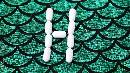 Obraz na płótnie Alphabet made of pills on a green and black background. Vitamins on a background of scales. Abc from drugs. Letter H made from pills. Capital letter H of medicines w salonie
