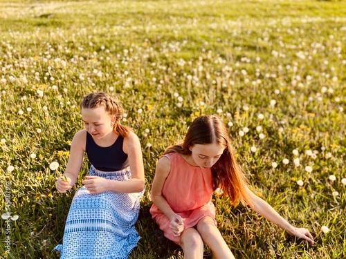 two teenage sisters  in summer dresses blowing dandelions in danelion meadow