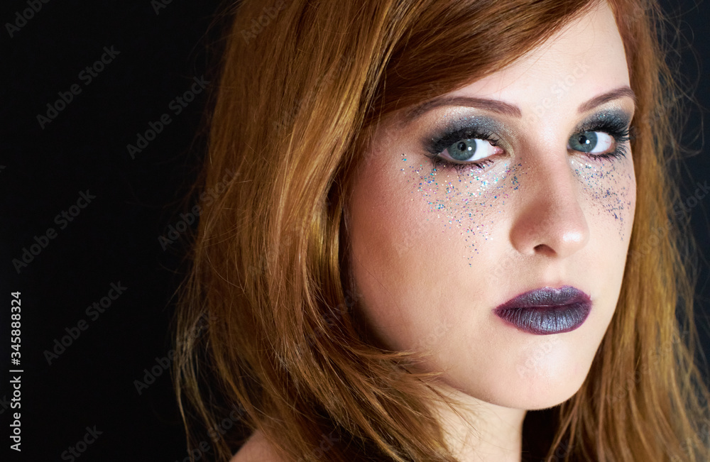 Young dazzling red headed woman with dark make up mascara and lip color, wearing metallic colorful glitter under her gray eyes and looking confident into camera. Young dazzling red headed woman with dark make up mascara and lip color, wearing metallic colorful glitter under her gray eyes and looking confident into camera.