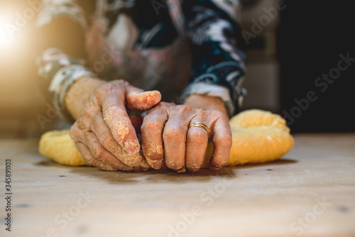 Close-up of old floured hands kneading dough to prepare fresh homemade pasta on a wooden cutting board. Italian old woman.