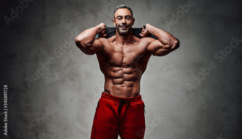 Canvas Print Close-up photo of a shirtless sportsman, flexing with a sand bag in a dark studi
