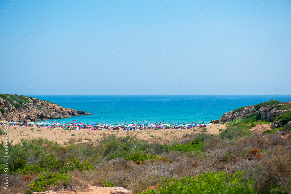 Beach in Sicily, Italy. People swiming in turquoise blue sea water and sunbathe in the sun. Summer vacation, lifestyle, recreation.