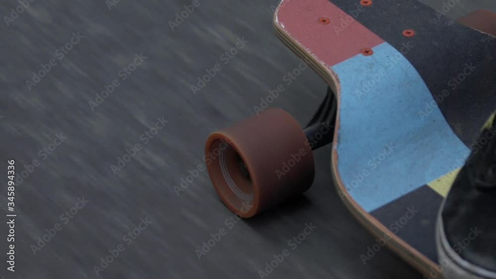 Closeup shot of man in black sneakers or skaters shoes rides longboard on asphalt or city tarmac.