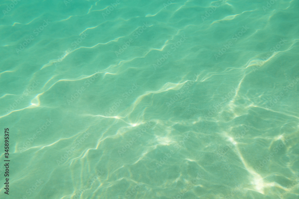 Underwater. Sun glare at the bottom of the sea. Waves underwater and rays of sunlight shining through. Deep turquoise blue sea. Ocean. Transparent water and light at sand.