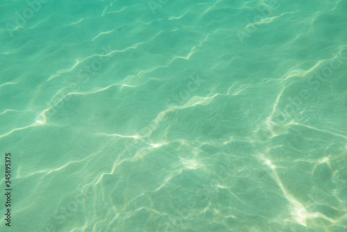 Underwater. Sun glare at the bottom of the sea. Waves underwater and rays of sunlight shining through. Deep turquoise blue sea. Ocean. Transparent water and light at sand.