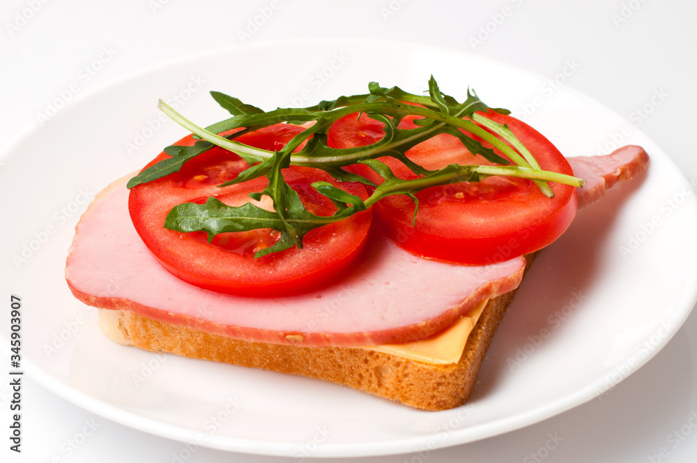 Sandwich of balyk, cheese, bread, tomatoes and arugula on a white plate on a plate view from the side