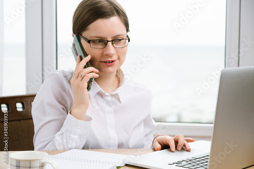 Woman talking by phone and using touchpad on laptop.