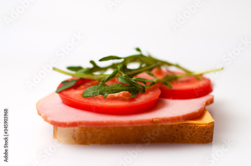 Sandwich made of balyk, cheese, bread, tomatoes and arugula on a white plate side view