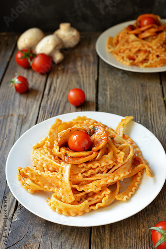 Pasta in a white plate. Pasta with tomato sauce, mushrooms with cherry tomatoes. Wooden background. Free space for text. Vertical view