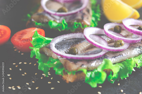 Appetizing smorrebrod with Norwegian herring, lettuce, blue onion, lemon and tomato lies on a wooden board