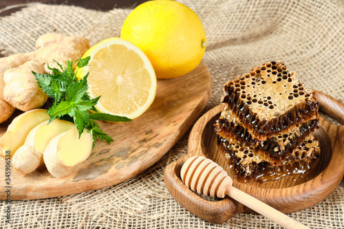 Fototapeta Naklejka Na Ścianę i Meble -  honey in honeycombs on a wooden plate and honey with nuts with lemon and ginger in rustic style on a wooden background. Close-up