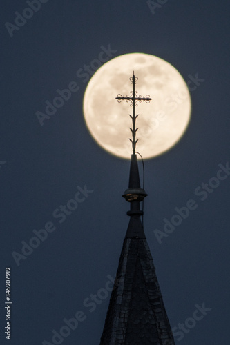 Church tower with cross in front of the super moon