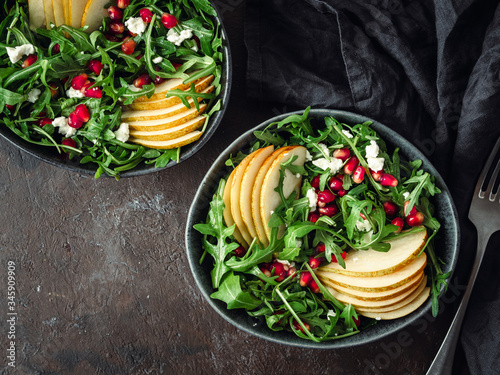 Vegan salad bowl with arugula, pear, pomegranate, coconut crumble or cottage cheese on black background. Vegan breakfast, vegetarian food, diet concept. Top view or flat lay. Copy space for text.
