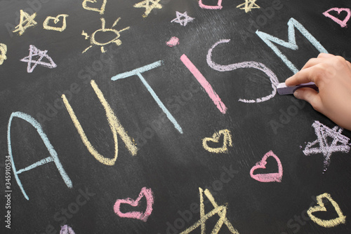 partial view of woman writing word autism on chalkboard