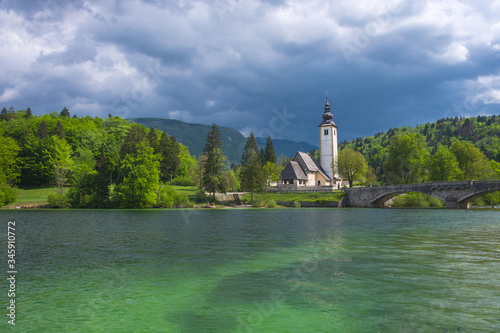 The charming little Church of St. John the Baptist on lake Bohinj, Julian Alps, the largest permanent lake in Slovenia. Beautiful spring colors, clear waters and dramatic sky