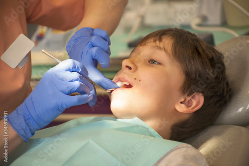 Dentist in blue gloves looks at the boy s teeth with a mirror in the clinic
