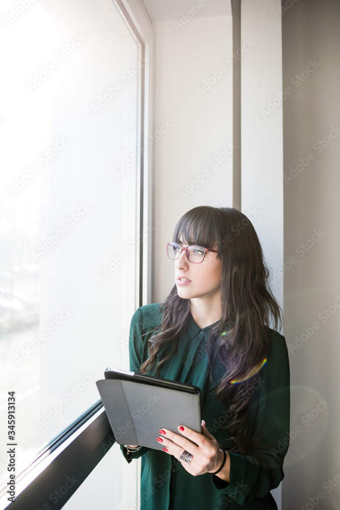 Young beautiful caucasian business woman standing near window indoors holfing tablet Young beautiful caucasian business woman standing near window indoors holfing tablet