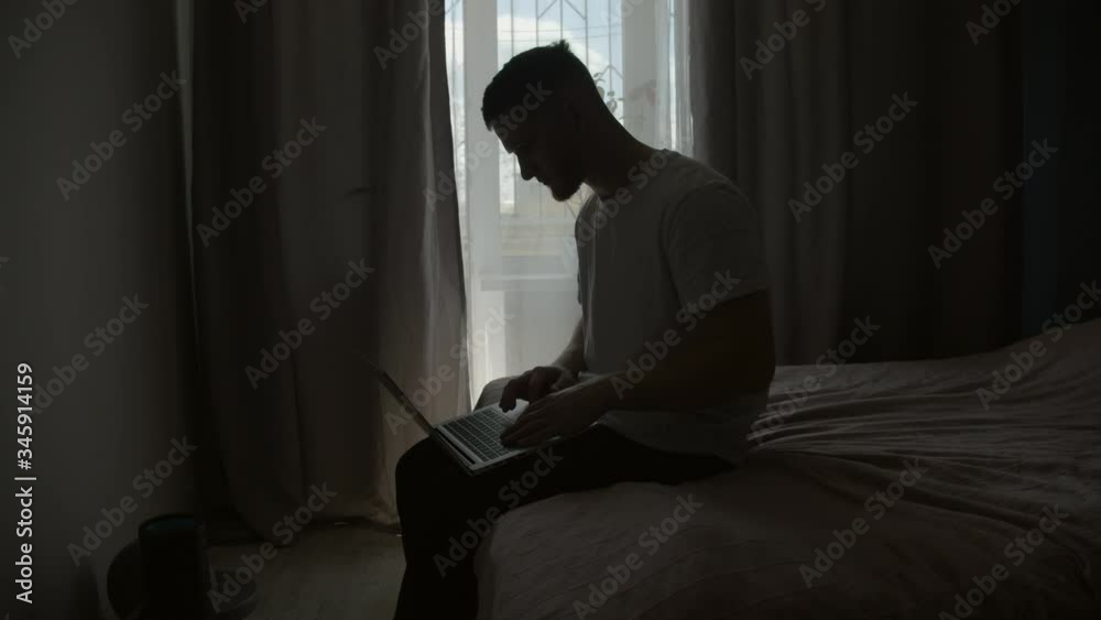 handsome guy typing on a laptop in a living room on a bed handsome guy typing on a laptop in a living room on a bed