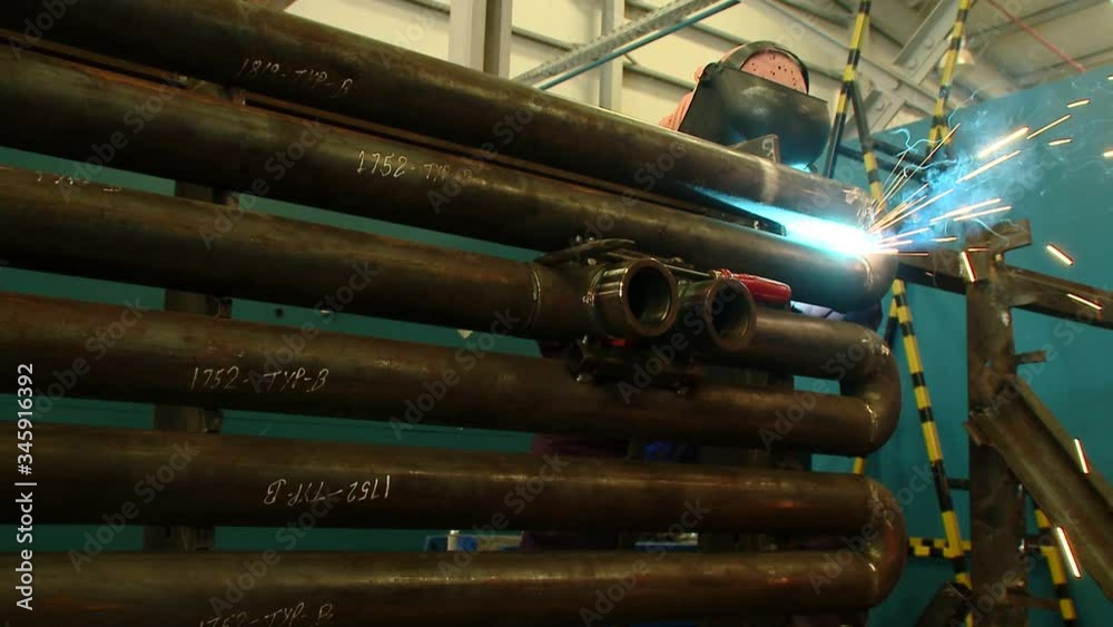 Reverse zooming in shot of a welder welding big pipes in a factory with intense light and sparks emitting from the operation Reverse zooming in shot of a welder welding big pipes in a factory with intense light and sparks emitting from the operation