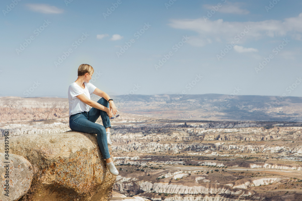 Traveler young woman sitting on a rock on mountain top with beautiful view under horizon, adventure