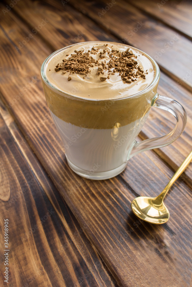 Dalgona coffee in the glass cup in the brown wooden background. Location vertical. Dalgona coffee in the glass cup in the brown wooden background. Location vertical.