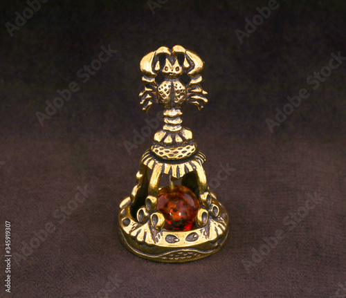 Amber souvenir. A miniature metal bell in the form of a zodiac sign "Cancer" with an amber element. Background is dark brown or white (isolated image).