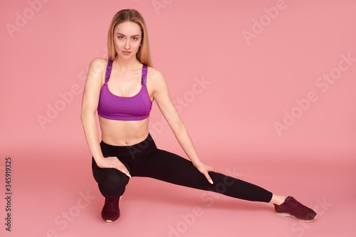 Girl doing side lunges stretching legs, studio shot. Pink background