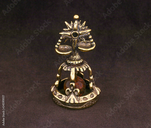 Amber souvenir. A miniature metal bell in the form of a zodiac sign "Libra" with an amber element. Background is dark brown or white (isolated image).