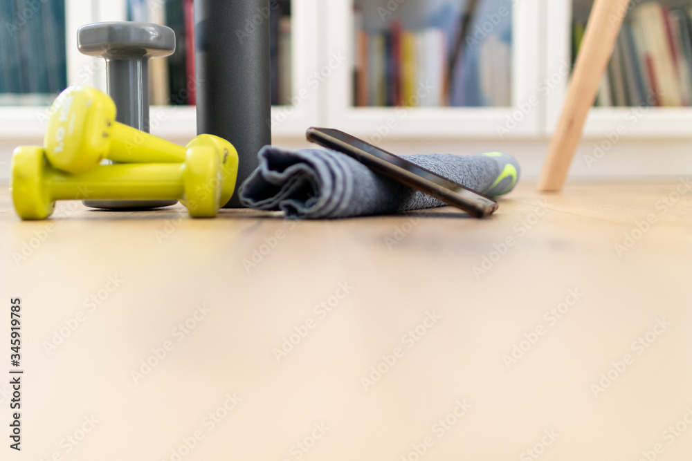Fitness at home, equipment and tools for gym at home. Dumbbell with towel, mobile phone and water, protein bottle on wooden parquet floor. Background copyspace sport activity at home with accessories.