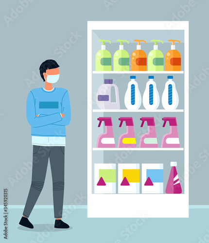 Young hipster wearing face medical mask standing near shelves with detergents in the supermarket. Man keep rules of quarantine during viral pandemic. Guy choose antibacterial agent in shop