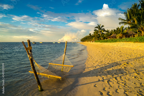 Fototapeta Naklejka Na Ścianę i Meble -  A hammock on the beach against a background of clouds, the ocean and an incredible sunset. Mauritius Island