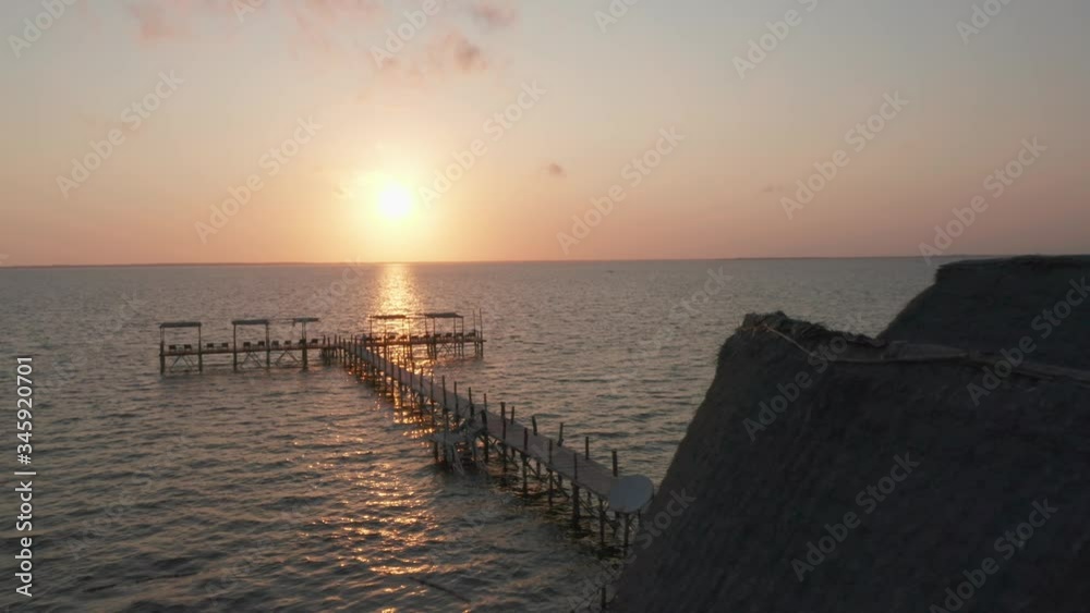 Aerial drone shot during sunrise flying forward close to a cabin over a pier in Zanzibar, Tanzania.