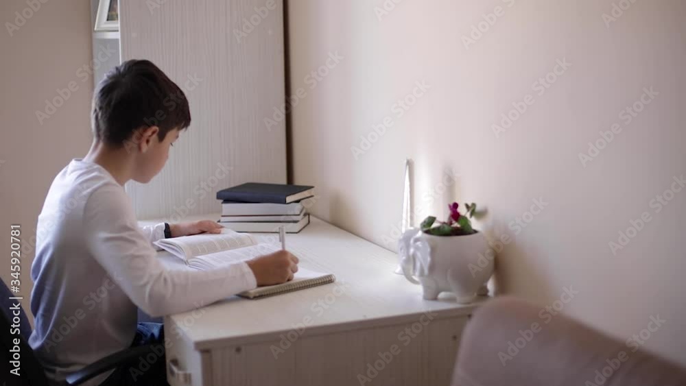 Young boy sitting at desk and read the book. Study at home during quarantine Young boy sitting at desk and read the book. Study at home during quarantine