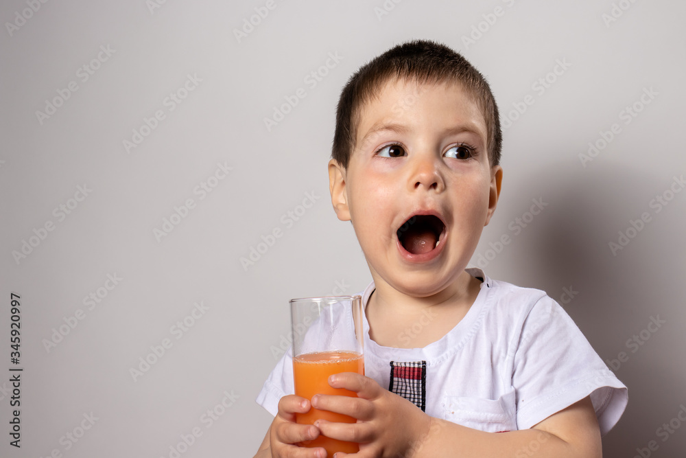 Little boy holds a glass of fruit juice. Vitamins for children, healthy baby food. The child opened his mouth. Little boy holds a glass of fruit juice. Vitamins for children, healthy baby food. The child opened his mouth.