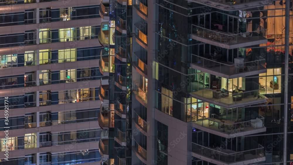 Rows of glowing windows with people in the interior of apartment buildings at night. Modern skyscrapers with reflections from glass surface. Concept for business and modern life Rows of glowing windows with people in the interior of apartment buildings at night. Modern skyscrapers with reflections from glass surface. Concept for business and modern life