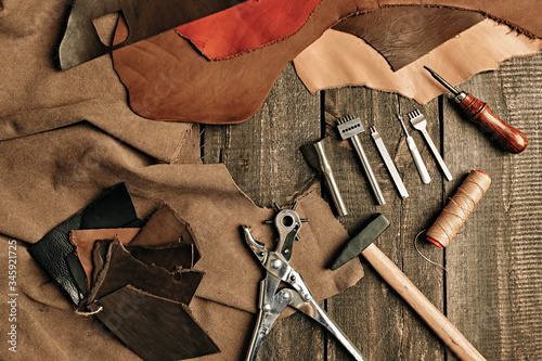 Flat lay composition with leather samples and set crafting DIY tools on wooden table background texture. Leather craftmans work desk. Copy space, maintenance concept. Belt goods production. Top view. photo