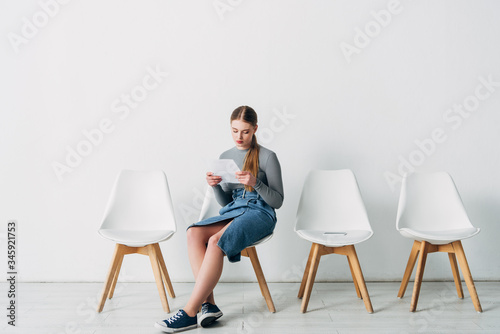 Attractive employee reading resume near smartphone on chair in office