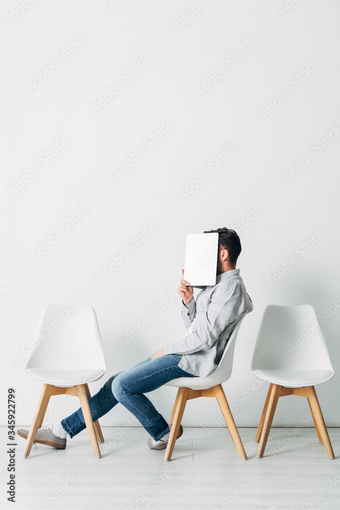 Fototapeta premium Side view of employee covering face with laptop while sitting on chair